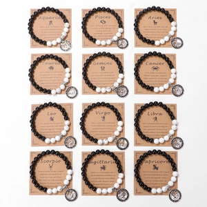 Set of 12 zodiac bracelets with black matte beads and symbolic charms on kraft cards