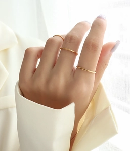 Three minimalist thin 18k gold rings stacked on finger with a white suit background
