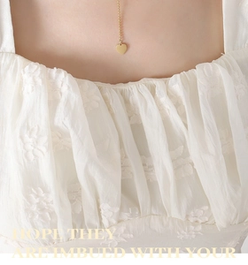 Detail of a golden heart pendant necklace on a model wearing a white ruffled top