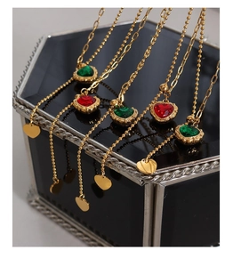 Detail of gold heart pendant necklace with red and green zircon on black box