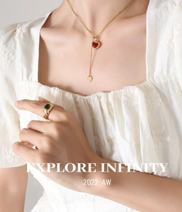 Detailed shot of golden heart necklace with red gemstone and green stone ring on model