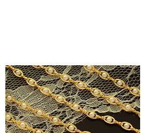 Detail of gold-plated chain links featuring inlaid white pearls on black background