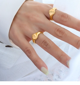 Detailopname van een goudkleurige brede ring met roosgravure aan de vinger op witte stof