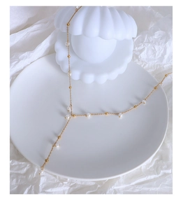 Vue détaillée du collier de perles dorées sur un plat en coquillage et papier blanc