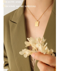Close-up of gold plated square S pendant necklace worn on a green blazer outfit