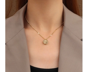 Close-up of golden Chinese Fu pendant necklace worn with a stylish khaki blazer