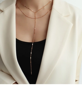 Detailed view of a double-layered rose gold Y-shaped necklace with long tassel metallic pendants