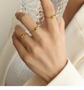 Gros plan de trois bagues chaînes minimalistes plaquées or 18k avec perles sur la main