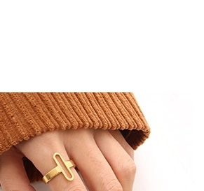 Gros plan d'une bague géométrique dorée ajourée portée sur une manche de pull en tricot orange
