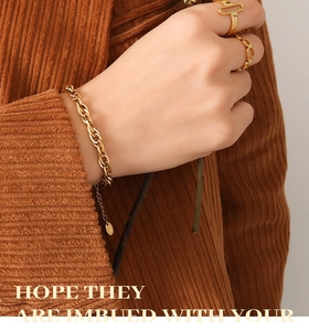 Détail d'un bracelet à grosse chaîne dorée et de bagues géométriques portés par un modèle