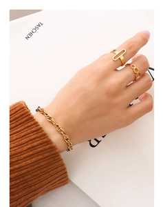 Détail de bracelet à grosse chaîne dorée et bagues géométriques sur velours côtelé