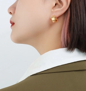 Close-up of gold-plated C-shaped hoop earrings with star patterns and zircon inlays