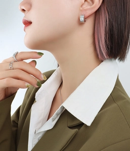 Close-up of silver C-shaped hoop earrings with zircon stars and minimalist rings