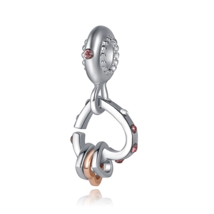 Detailed macro of a heart-shaped silver charm with pink zircon and rose gold interlocking rings