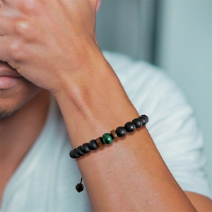 Dettaglio del bracciale con perle nere opache, occhio di tigre verde e legno
