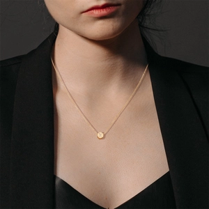 Close-up of minimalist 18K gold chain necklace with a round letter X pendant for women