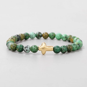 Close-up of 6mm green natural stone beads and polished golden cross charm on elastic bracelet