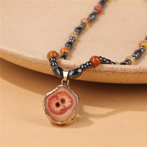 Close-up of agate slice pendant with hematite and red beads on a ceramic vessel