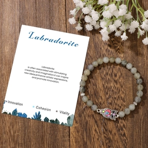 Dettaglio delle perle in labradorite e ciondolo a gufo su sfondo di legno scuro
