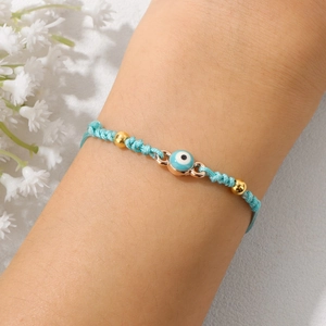 Detail eines handgewebten hellblauen Evil Eye Armbands mit Goldperlen am Handgelenk