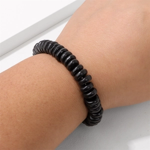 Bracciale di perle di legno nere lucide con cordino elastico su sfondo minimalista