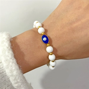 Primer plano de pulsera de cuentas mal de ojo con bolas blancas y detalles dorados en la muñeca