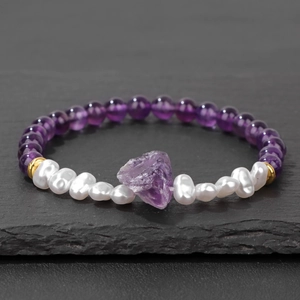 Detail van 6mm amethist kralenarmband met barokparels en ruwe kristalsteen op rots