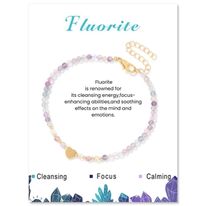 Macro detail of 3mm faceted fluorite beads with a gold heart pendant on white card
