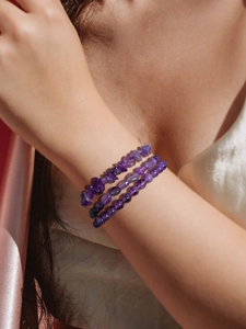 Detailed shot of three purple amethyst crystal bracelets on a soft silk background