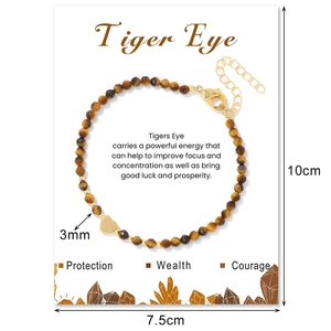 Detailed macro view of 3mm faceted tiger eye beads and golden heart charm on a card