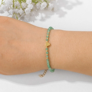 Detail of 18k gold beaded bracelet featuring green stones and a gold heart charm