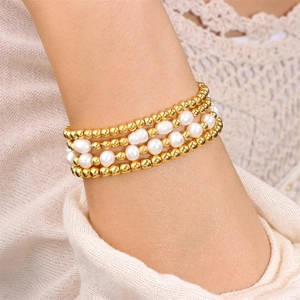 Gros plan de bracelets de perles dorées et de perles d'eau douce blanches sur poignet