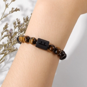 Gros plan du bracelet en perles d'oeil de tigre et agate noire porté au poignet