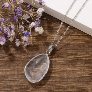 Detail of faceted drop crystal pendant with silver bezel on dark wooden surface with flowers