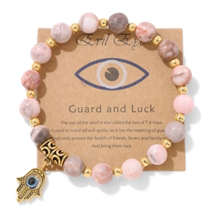 Détail de perles en marbre rose avec breloque Main de Fatma dorée et Mauvais Œil sur carte