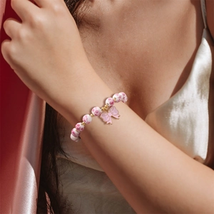 Floral ceramic beaded bracelet with a pink enamel bow charm on a model's wrist