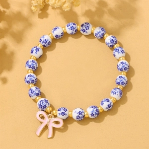 Close-up of blue and white floral ceramic beads with a pink bow charm on a beaded bracelet