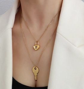 Detail of 18k gold double-layer necklace with heart lock and engraved key pendant on model