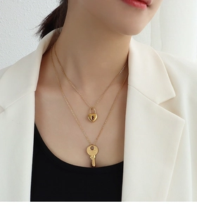 Detail shot of a double-layered gold necklace featuring heart lock and key pendants
