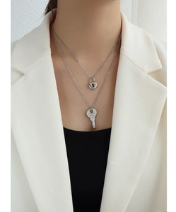 Detail of silver double-layer necklace with heart lock and engraved key pendants on model