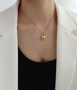Close-up of golden heart lock pendant necklace worn with a white blazer for a chic look