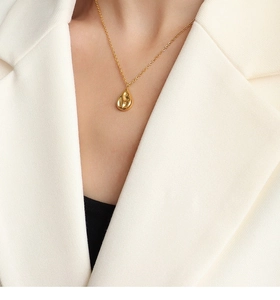 Detailweergave van een gouden druppelvormige hanger aan een ketting op een blazer