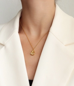 Close-up van de gouden druppelvormige hanger aan een ketting bij een witte blazer