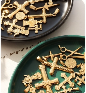 Detailed close-up of 18K gold plated titanium steel cross and scissor pendants in a dish