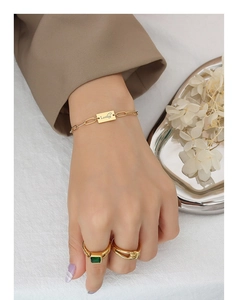 Primo piano del bracciale dorato Lucky e dell'anello con gemma verde sulla modella