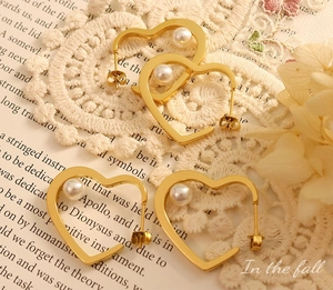 Detail view of gold heart pearl earrings resting on vintage paper and lace background