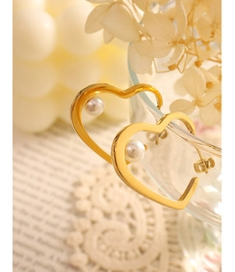 Close-up of heart-shaped gold-plated earrings with white pearls on a glass rim