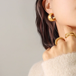 Élégantes boucles d'oreilles créoles C dorées et bagues texturées sur un mannequin