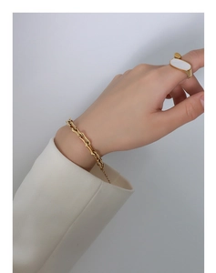Détail du bracelet à maillons dorés en U et de la bague ovale portés sur le poignet