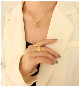 Primo piano di una collana a maglie dorate e anelli testurizzati con un abito beige